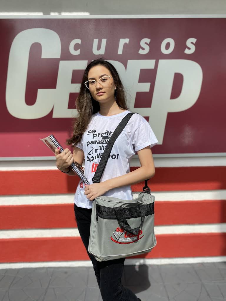 Aluna do CEDEP em frente à fachada da escola, com caderno e mochila.