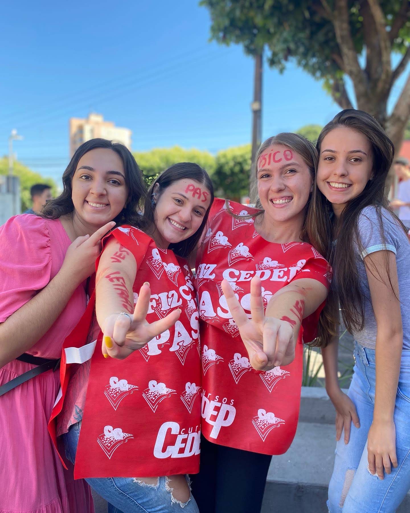Quatro alunas comemoram fazendo sinal de vitória, com o nome dos cursos pintado na testa e nos braços.