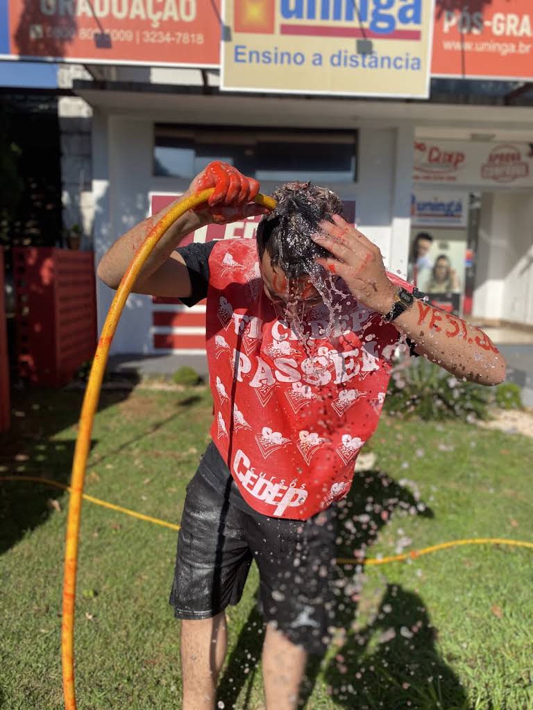 Aluno aprovado sendo molhado com a mangueira durante a comemoração.