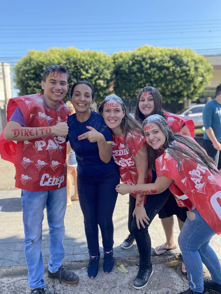 Alunos aprovados abraçados com a professora, todos sujos de farinha.